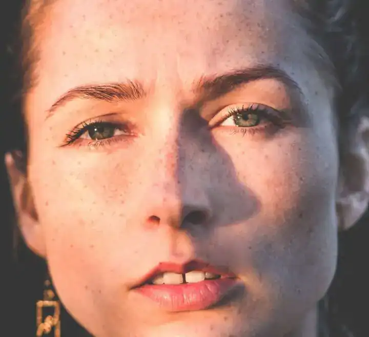 freestocks-vjvlne0twi-unsplash-720x657-jpg Närbild på en ung kvinna med fräknar och gröna ögon, naturligt solljus som framhäver hennes ansiktsdrag och betonar självförtroende och äkthet för bedömning och personlighetstestning.