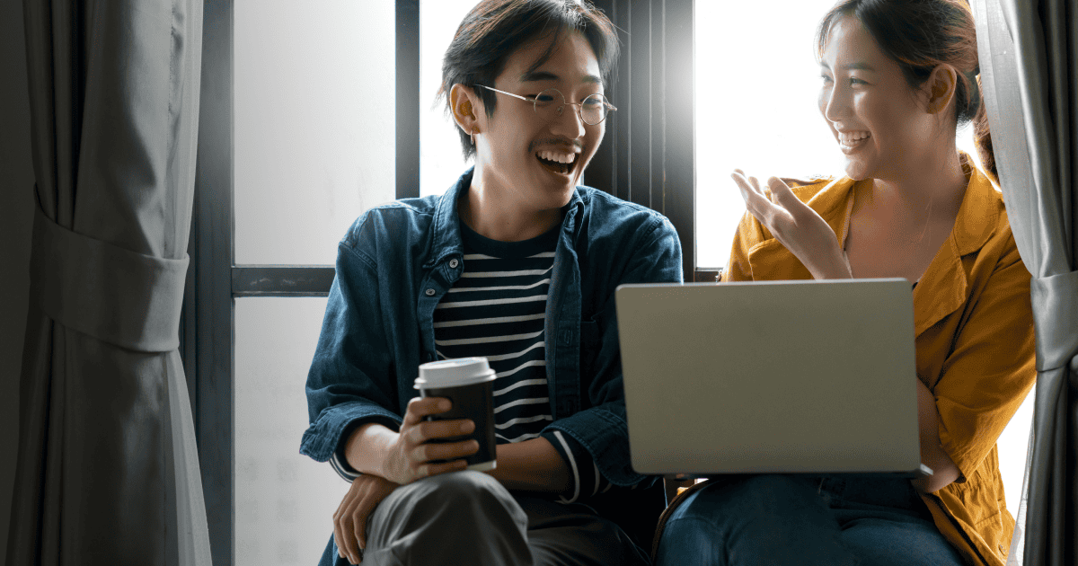 Two young women collaborating and sharing ideas using a laptop and smartphone, representing teamwork and digital communication in a professional setting.